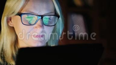一个年轻女人的肖像，特写。 与平板电脑一起工作，屏幕反映在她的眼镜上